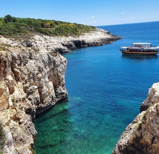 A scenic view of cliffs and turquoise waters with a boat anchored in a cove.