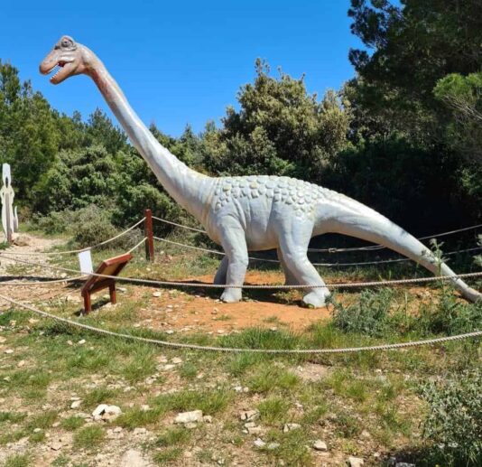 A life-sized dinosaur model of a Brachiosaurus on display in Dinopark surrounded by greenery.